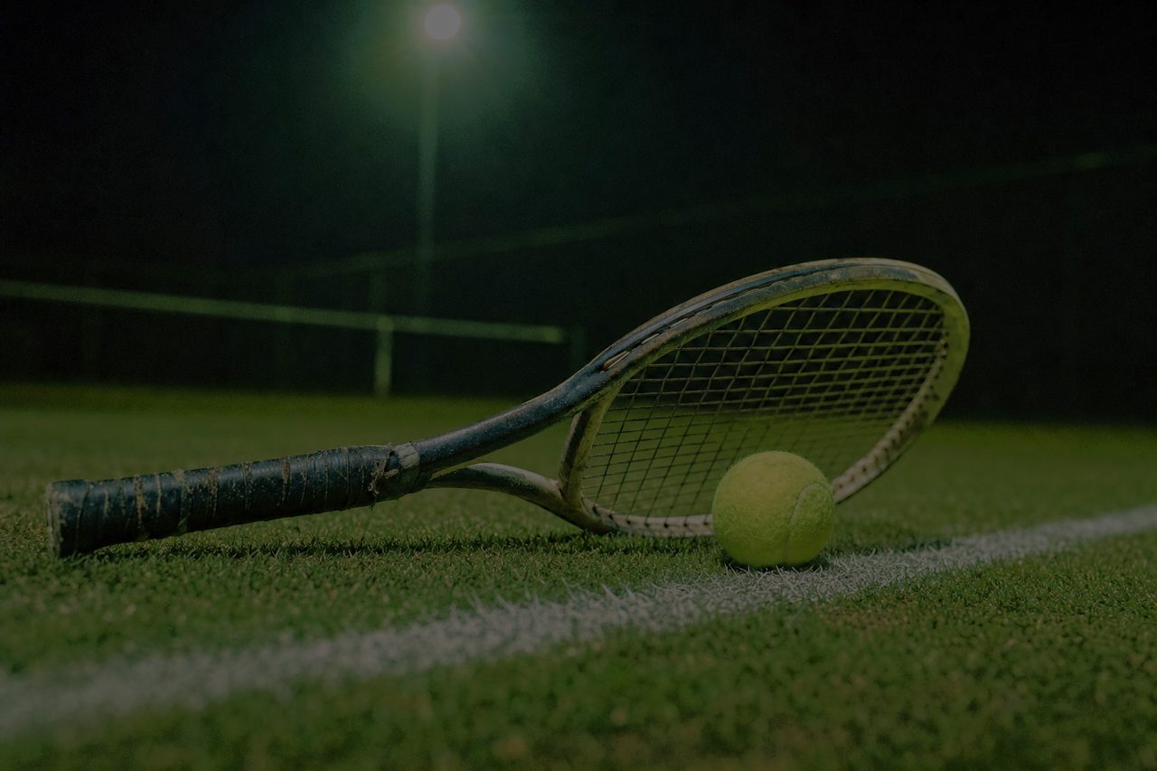Tennisschläger und Ball auf der Grundlinie eines Rasenplatzes bei Flutlicht